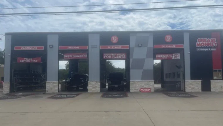 Exterior of a Grease Monkey oil change shop with four service bays, each labeled for different automotive services, and two vehicles inside.
