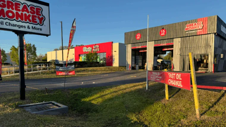 A Grease Monkey oil change service center with open service bays and a nearby O'Reilly Auto Parts store on a clear day.