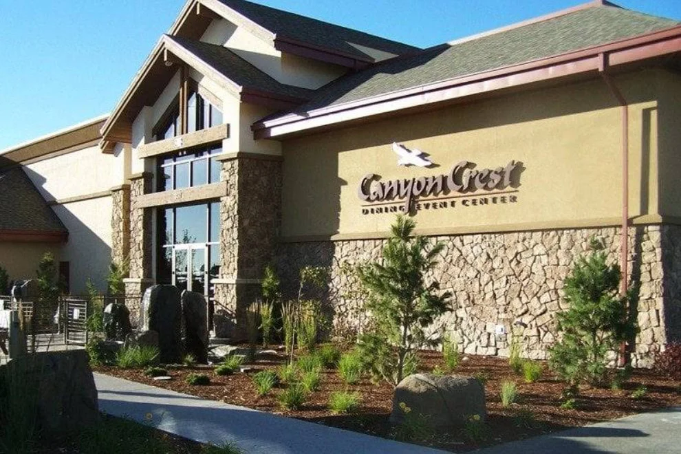 Exterior view of Canyon Crest Dining & Event Center in Twin Falls Idaho with stone facade, large windows, and landscaped plants and trees.