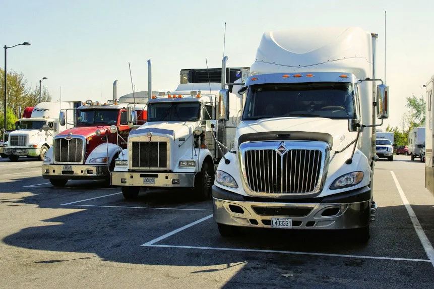Several semi-trucks are parked in a row at a truck stop parking lot in Idaho Falls on a sunny day, reflecting the importance of engine and oil care for long-haul journeys.