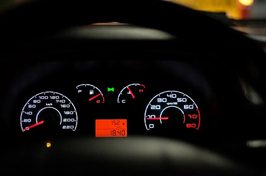 Close-up of a car dashboard showing speedometer, fuel gauge, temperature gauge, and odometer illuminated at night. Perfect reminder for regular oil changes and car maintenance in Rexburg. Digital display shows 18,407 miles and 15.2°C.