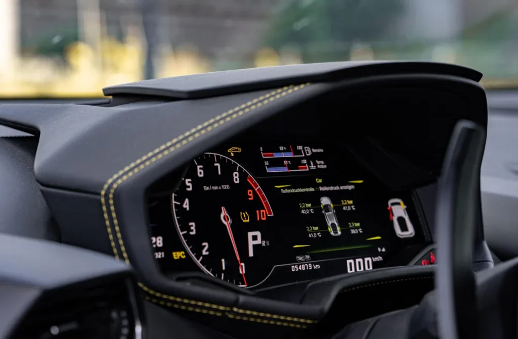Close-up of a digital car dashboard displaying speed, RPM, warning lights, and various status indicators with yellow contrast stitching on the instrument panel—perfect for tracking vehicle maintenance or scheduling oil changes in Pocatello Idaho.