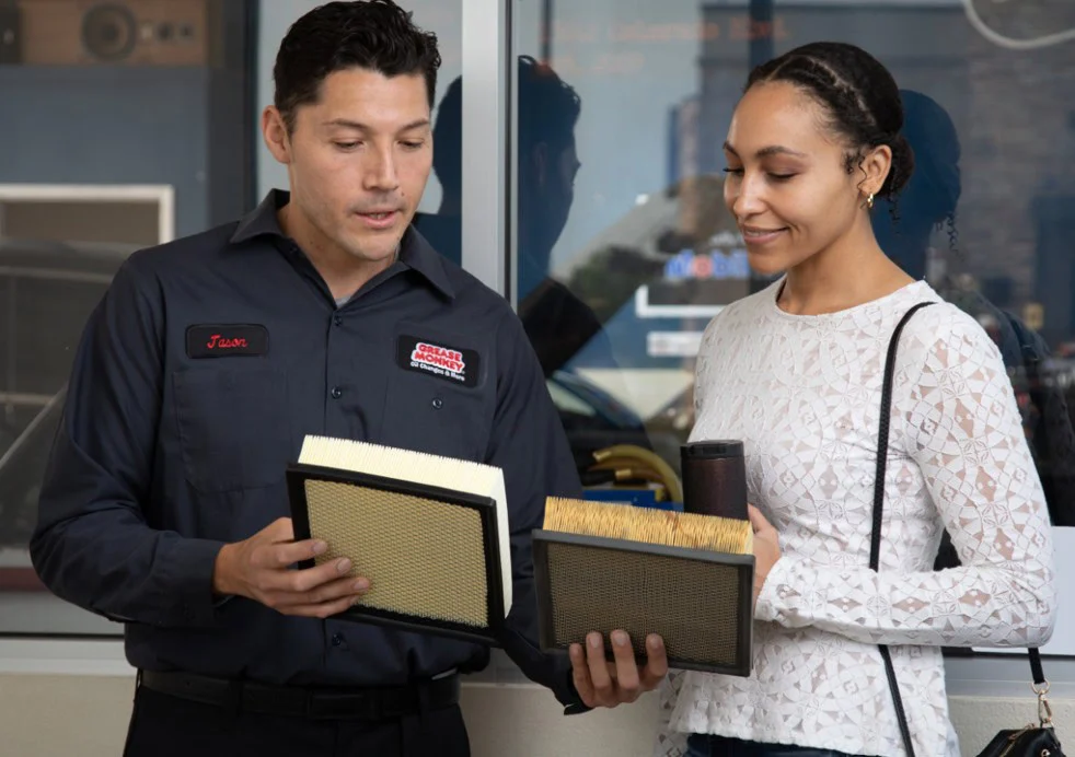 At Grease Monkey in Jerome, Idaho, an auto mechanic shows a customer two car air filters, comparing them and discussing options to ensure engine long life inside the repair shop.