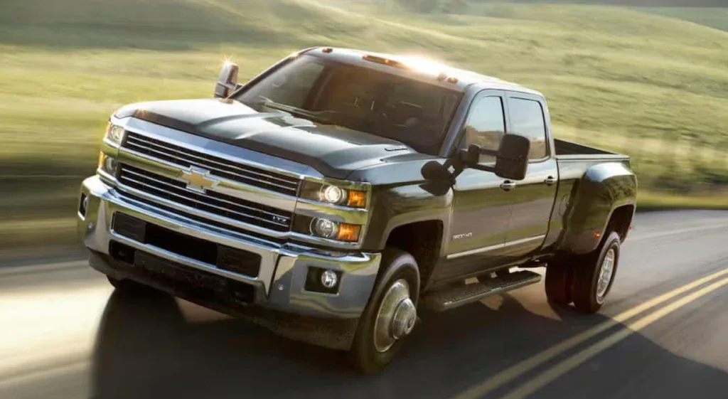 A large silver Chevrolet pickup truck, known for its engine long life, drives on a paved rural road with grassy hills in the background near Jerome, Idaho.