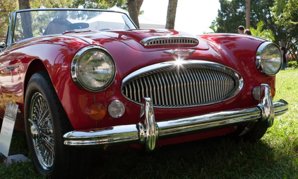 A classic red convertible car is parked on grass in Rexburg, with sunlight reflecting off its chrome grille and bumper—a perfect example of how regular car maintenance, like timely oil changes, keeps vehicles shining and road-ready.