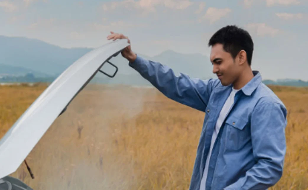 A man standing outdoors in a field near Twin Falls, Idaho, opens the hood of a steaming car, appearing to inspect the engine for potential issues and ensure proper engine protection.
