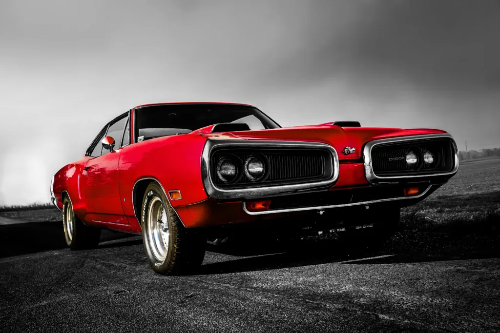 A red classic muscle car is parked on an empty outdoor road, its vibrant color contrasting with the black and white background—highlighting both vehicle safety and timeless style.