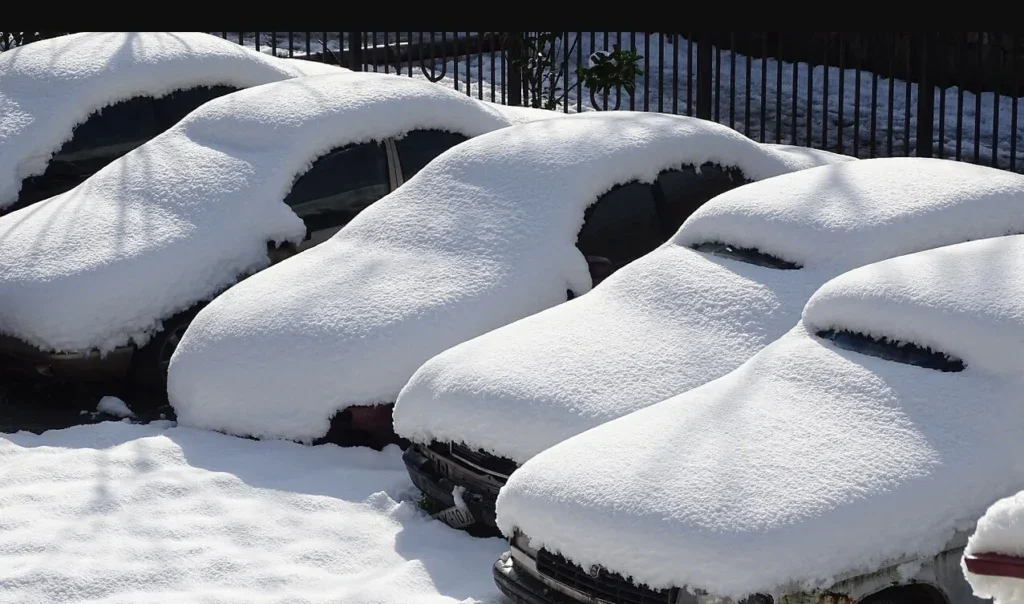 Four parked cars in Rexburg are covered in a thick layer of snow, with only parts of their windshields and front bumpers visible—a clear reminder that winter car maintenance and timely oil changes are essential.