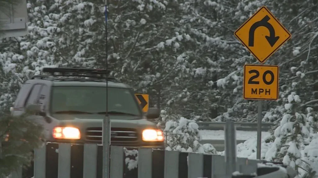 A green SUV drives on a snowy Twin Falls Idaho road past a yellow right-curve sign with a 20 MPH limit, enjoying peace of mind thanks to Grease Monkey oil change engine protection.