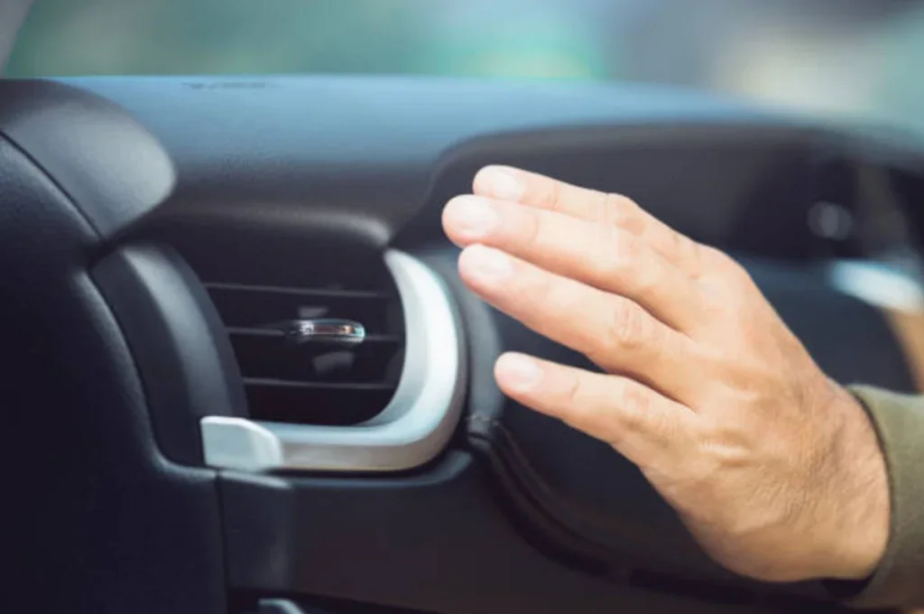 A hand is held in front of a car air conditioning vent inside a vehicle, checking the cool airflow after a visit to Channing Way Car AC Service.