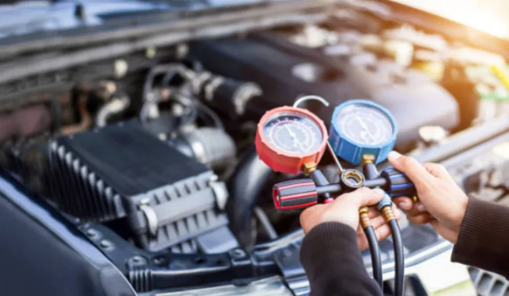 A person at Grease Monkey Pocatello uses a manifold gauge set to check the Car AC system of a car engine.