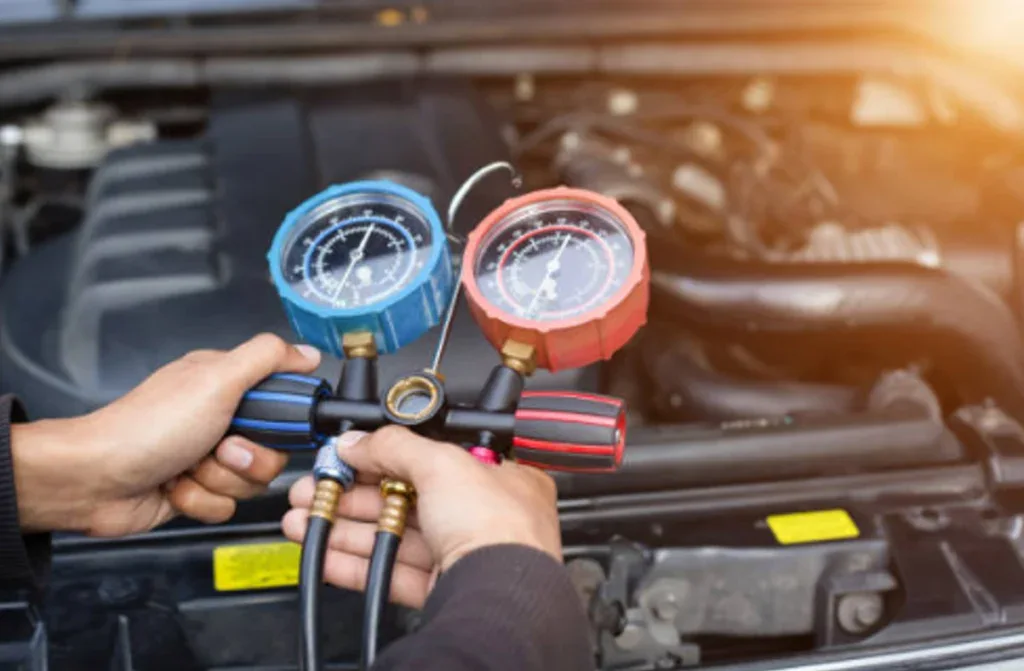A person holds HVAC manifold gauges to check the pressure of an automotive air conditioning system under an open car hood at Channing Way Car AC Service.