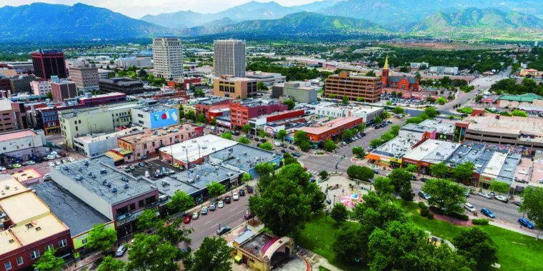 Aerial view of Colorado Springs with a mix of low-rise and high-rise buildings, tree-lined streets, mountains in the background, and bustling roads where drivers might be headed for an oil change or engine service.