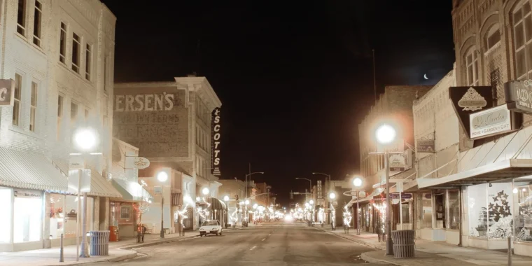 A nighttime view down a street lined with illuminated buildings and storefronts.