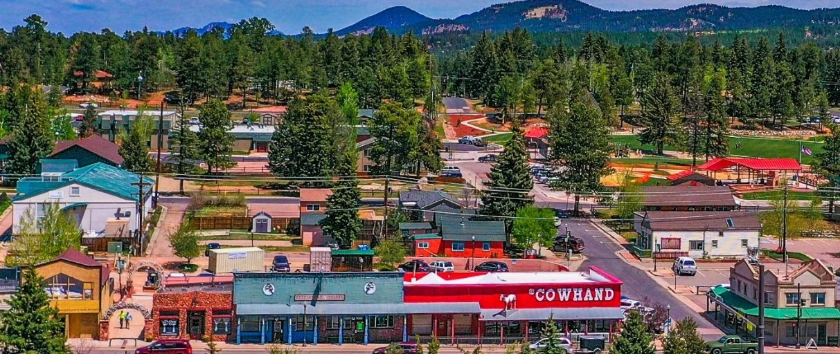 A small town with colorful buildings, trees, and mountains in the background; the main street features a red-and-white store called Cowhand.