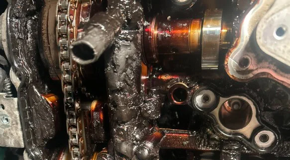 Close-up of an engine with a heavy buildup of black sludge and deposits on the chains and metal components—a clear example of why regular vehicle maintenance and timely oil change are essential.