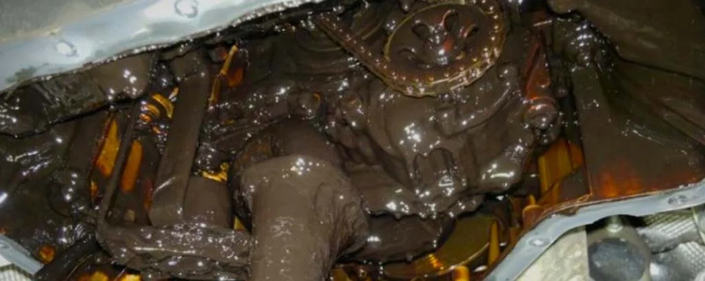 Close-up view of a Woodland Park engine interior covered in thick, dark sludge, suggesting oil contamination or neglect of a regular maintenance and oil change schedule.