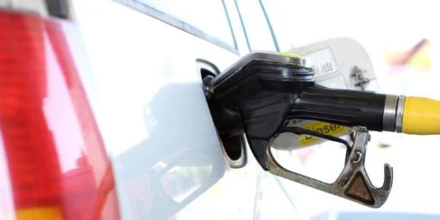 A yellow fuel pump nozzle is inserted into the fuel tank of a white vehicle at a gas station, highlighting the importance of regular vehicle maintenance Jerome Idaho.