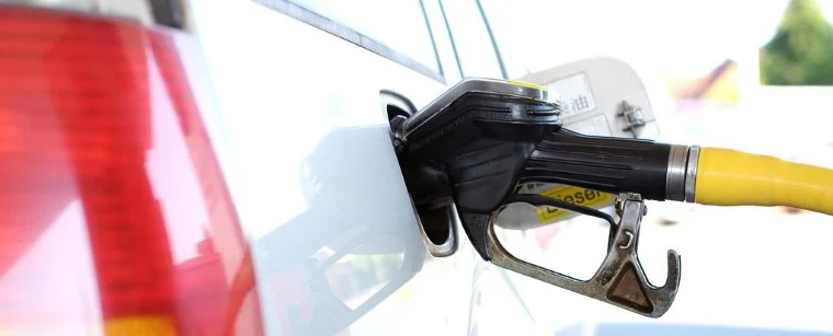 A yellow fuel pump nozzle is inserted into the fuel tank of a white vehicle at a gas station, highlighting the importance of regular vehicle maintenance Jerome Idaho.