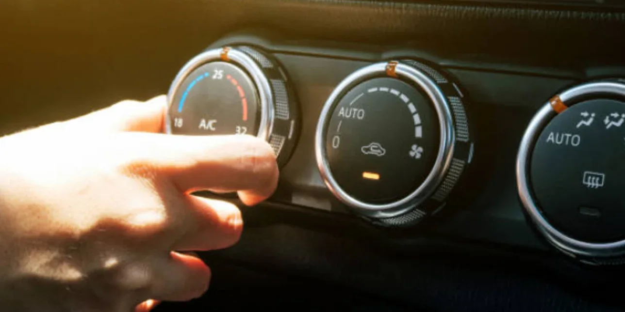A hand adjusts the air conditioning temperature dial on a car dashboard next to two other climate control knobs, exemplifying proper Car AC Care for drivers in North Holmes and Idaho Falls.