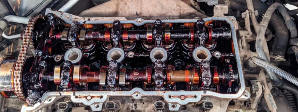 Close-up view of a car engine’s exposed cylinder head in Aurora, showing oily camshafts, valves, and timing chain—reminding residents of the importance of regular oil changes for clean and efficient engine parts.