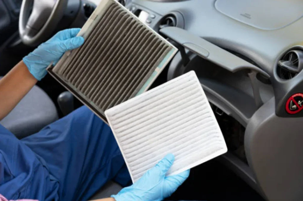 A person wearing blue gloves holds a dirty cabin air filter and a clean filter inside a car near the glove compartment, illustrating an essential step from the Chevy AC guide for maintaining your Twin Falls vehicle AC in top condition.