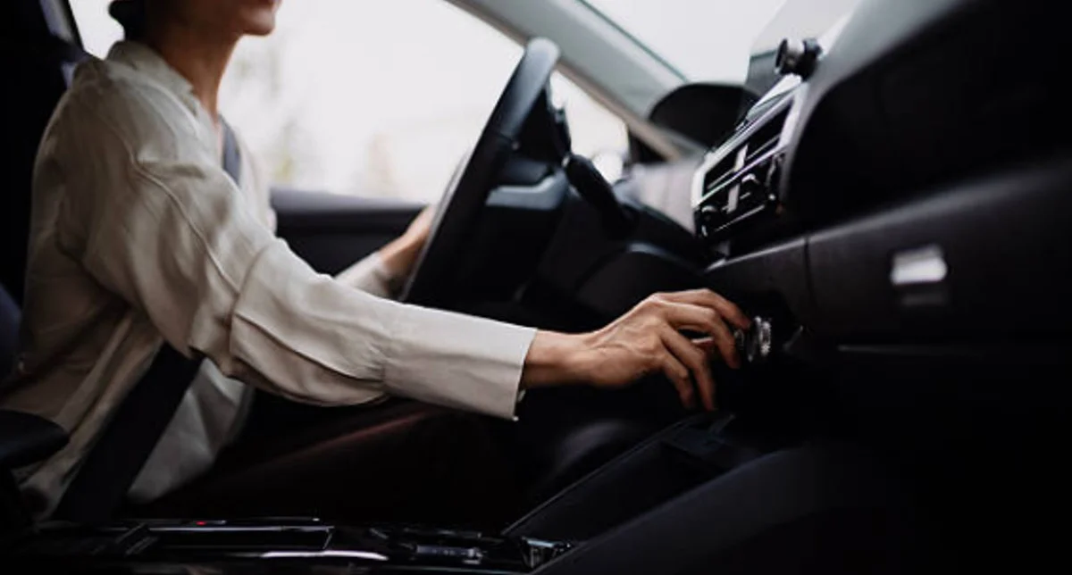 Jerome sits in the driver’s seat of his car, smiling as he reaches forward to adjust the dashboard controls, showing off his vehicle AC care after a visit to Grease Monkey.