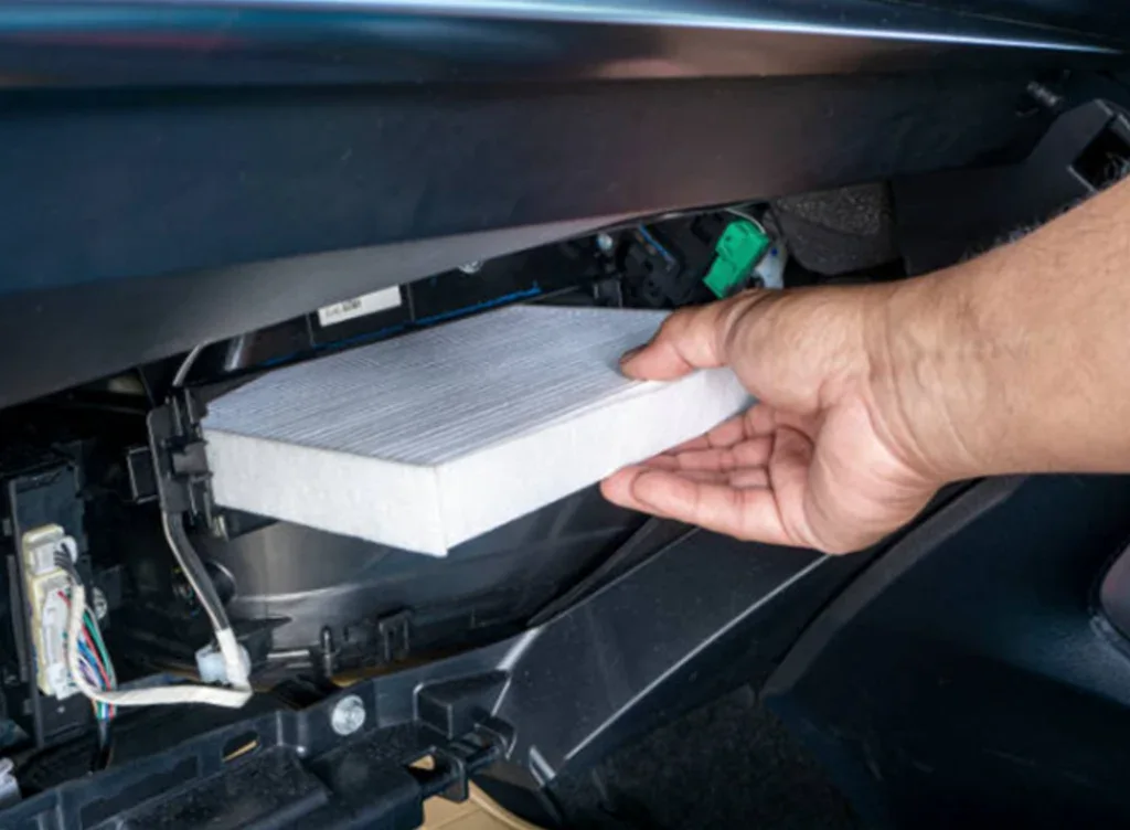 A person’s hand is installing or removing a rectangular air cabin filter from the compartment inside a car dashboard, demonstrating careful Car AC Care in Idaho Falls.