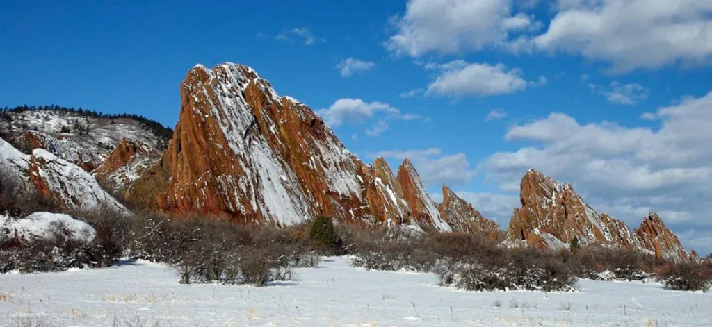 Jagged red rock formations rise from a snow-covered landscape under a partly cloudy blue sky, reminiscent of the reliability you can expect from a well-serviced Littleton engine with regular maintenance.