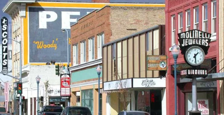 Downtown street with parked cars, historic brick buildings, business signs, and a vintage clock outside Molinelli Jewelers under a cloudy sky—drivers from Southeast Pocatello can also spot local shops offering vehicle air conditioning service.
