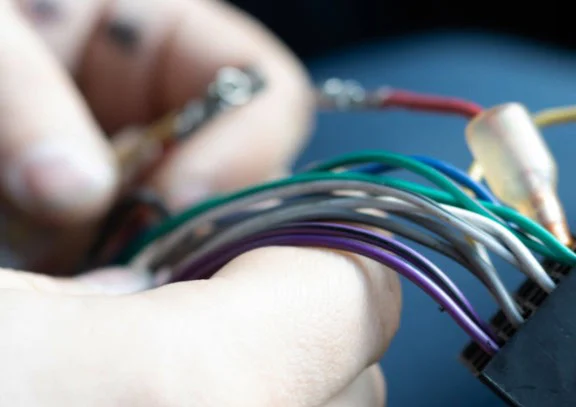 Close-up of a person’s hand holding several colored electrical wires, with a blurred background—perfect for illustrating vehicle air conditioning service tasks in Rexburg Idaho that drivers may need.
