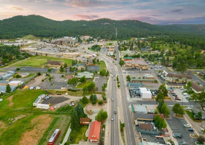 Aerial view of Woodland Park, Colorado—a small town with roads, cars serviced and inspected, buildings, and surrounding green hills under a partly cloudy sky.