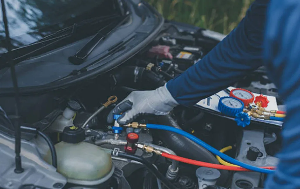 A mechanic provides air conditioning service using gauges and hoses to work on a vehicle air conditioning system under the open hood in Colorado Springs.