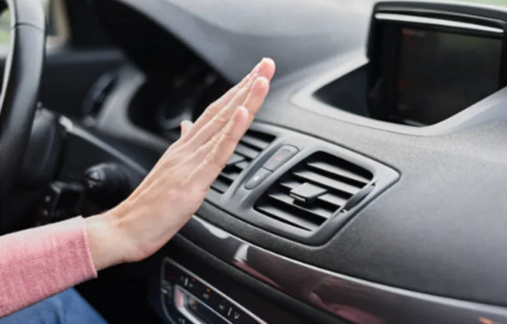 A person holds their hand in front of a car air vent on the dashboard, checking airflow inside the vehicle—an essential step before scheduling vehicle air conditioning service in Colorado Springs.