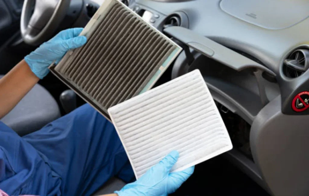 A person wearing blue gloves holds a dirty cabin air filter and a clean one inside a car near the glove compartment, highlighting the importance of vehicle air conditioning maintenance in Littleton Colorado.