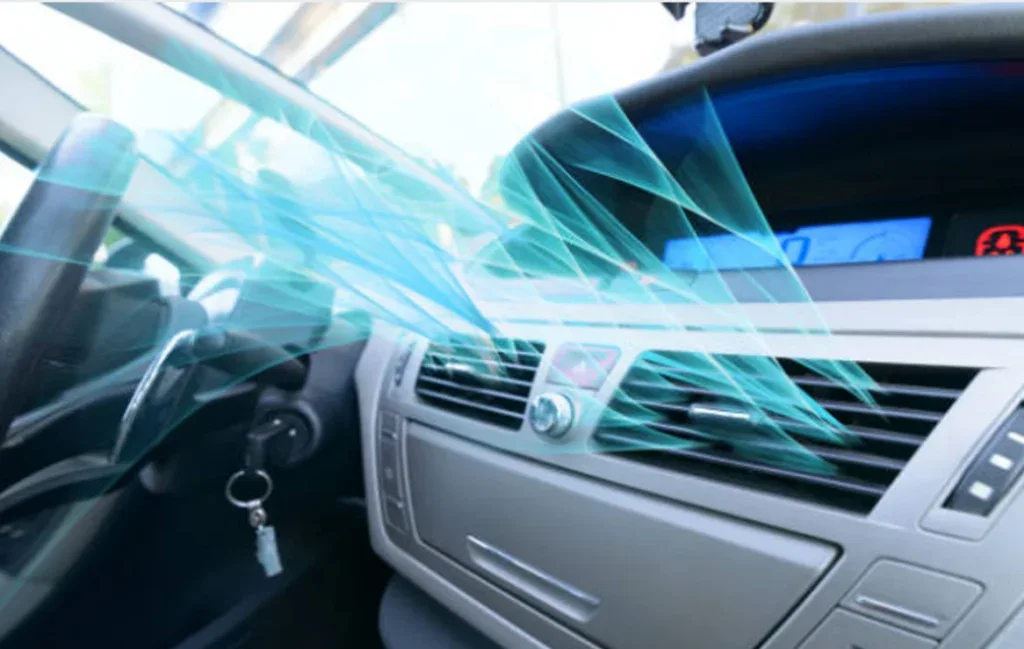 Car dashboard with digital display and air conditioning vent emitting illustrated blue airflow, showcasing interior climate control—perfect for managing Aurora Colorado vehicle air conditioning. Keys are visible in the ignition.