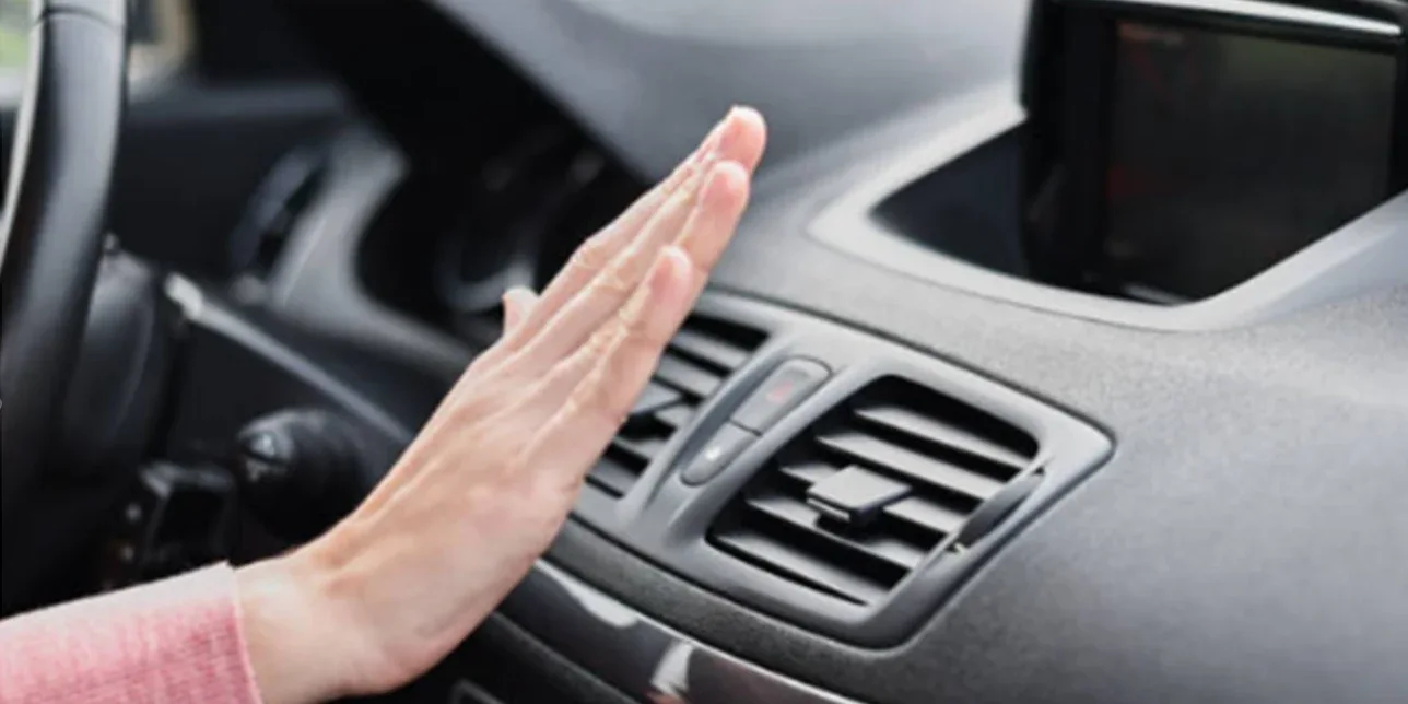 A driver holds their hand in front of a car’s air conditioning vent on the dashboard, checking airflow—reminding drivers in Rexburg Idaho of the importance of regular vehicle air conditioning service.