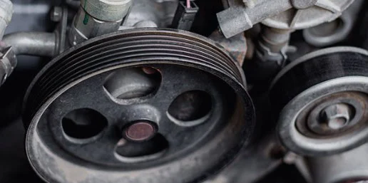 Close-up view of a car engine’s serpentine belt and pulleys, highlighting the mechanical components essential for vehicle air conditioning and emphasizing the importance of regular service in Pocatello, Idaho.