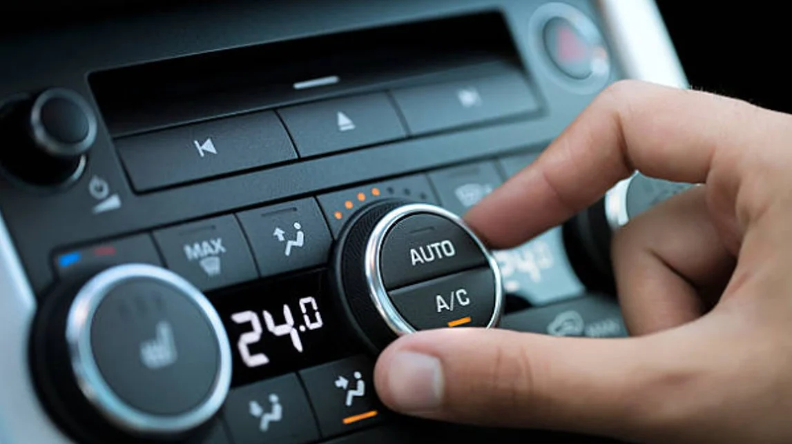 A hand adjusts the automatic climate control knob on a car dashboard, displaying a temperature setting of 24°C.