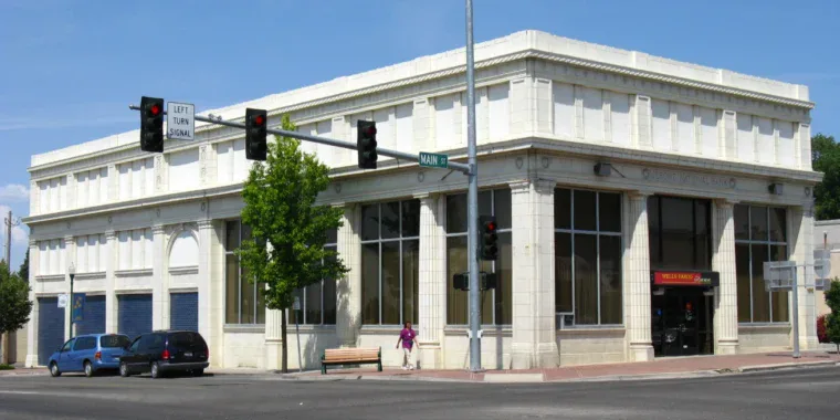 A two-story white stone bank building with large windows on a street corner in Jerome, Idaho, featuring a "Wells Fargo" sign, traffic lights, and nearby businesses offering vehicle air conditioning service.