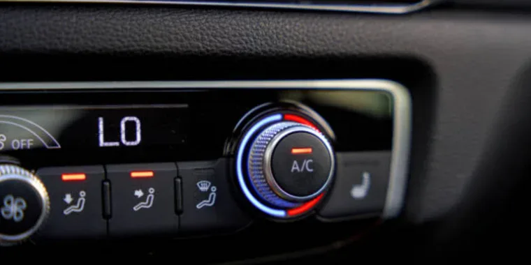 Close-up of a car climate control panel set to low temperature, with the A/C button illuminated and seat heating indicator visible.