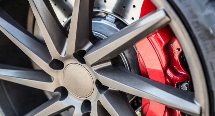 Close-up of a car wheel showing a dark metallic rim, red brake caliper, and ventilated disc brake—perfectly highlighting the importance of regular brake inspection and expert brake service in Colorado Springs.