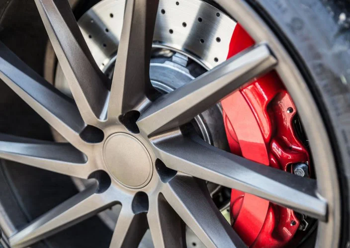 Close-up of a car wheel showing a dark metallic rim, red brake caliper, and ventilated disc brake—perfectly highlighting the importance of regular brake inspection and expert brake service in Colorado Springs.