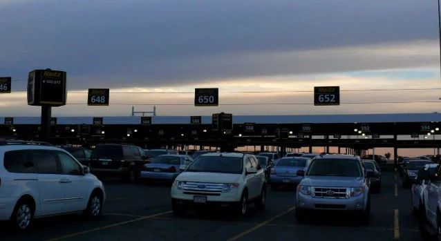Cars parked in rows at a rental car lot during sunset, with numbered signs above each row—a reminder of the importance of regular vehicle maintenance. The sky is partly cloudy with a faint glow near the horizon, creating an ideal backdrop for anyone considering reliable brake service Aurora to ensure their journey starts safely.