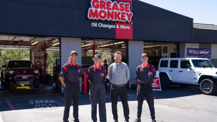 Four employees stand outside a Grease Monkey auto service shop in the South Metro area, with two vehicles parked in open service bays behind them.