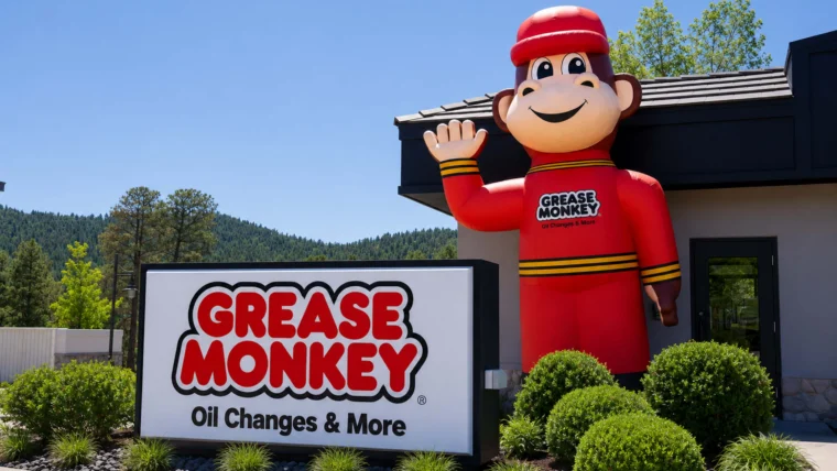A large inflatable monkey mascot stands next to a Grease Monkey automotive service center sign that reads, “Oil Changes & More,” welcoming customers across the Denver Metro and Front Range areas.