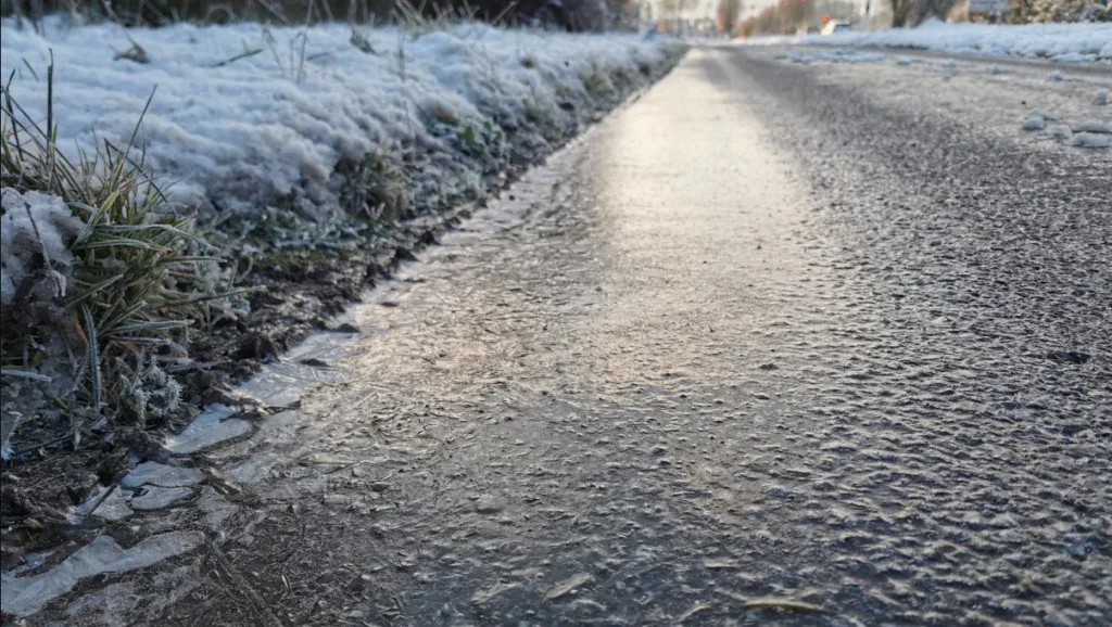 A close-up of an icy, frozen sidewalk bordered by snow-covered grass on a cold winter day—a reminder of how essential vehicle maintenance, such as brake system service at Grease Monkey Rexburg, can be when navigating treacherous winter roads.