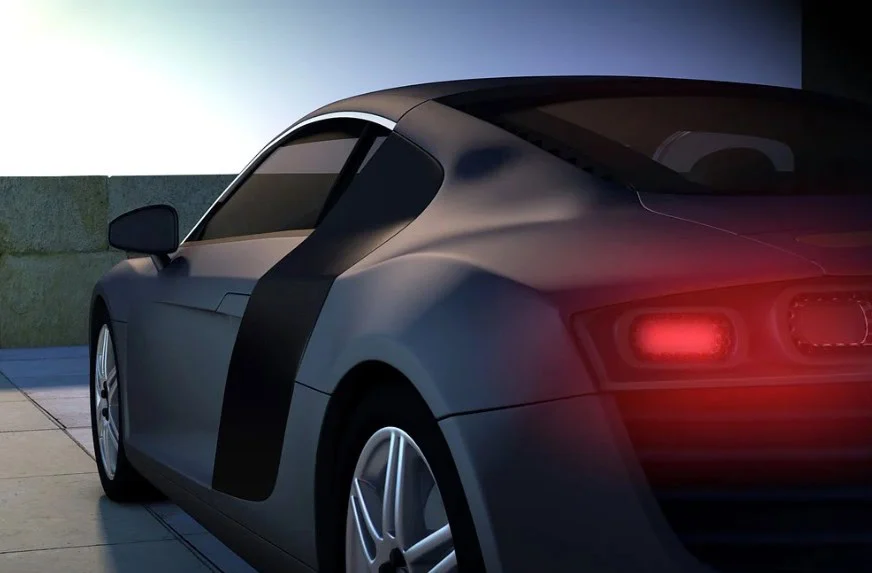 A sleek black sports car with its brake lights illuminated is parked outdoors on a tiled surface near a low wall at dusk, highlighting the importance of regular brake system repair and vehicle maintenance—services expertly provided by Grease Monkey Rexburg.