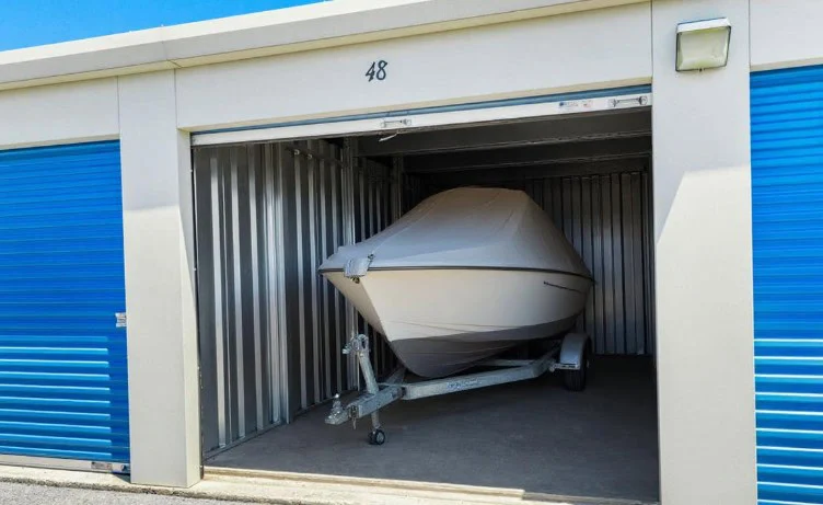 A covered boat on a trailer is stored inside a storage unit with a partially open blue door labeled 48 in Idaho Falls.