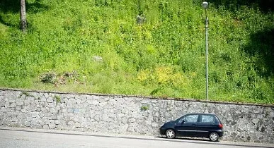 A small black car is parked on Business Loop in Rexburg beside a stone wall, with a grassy hill and a streetlamp in the background.